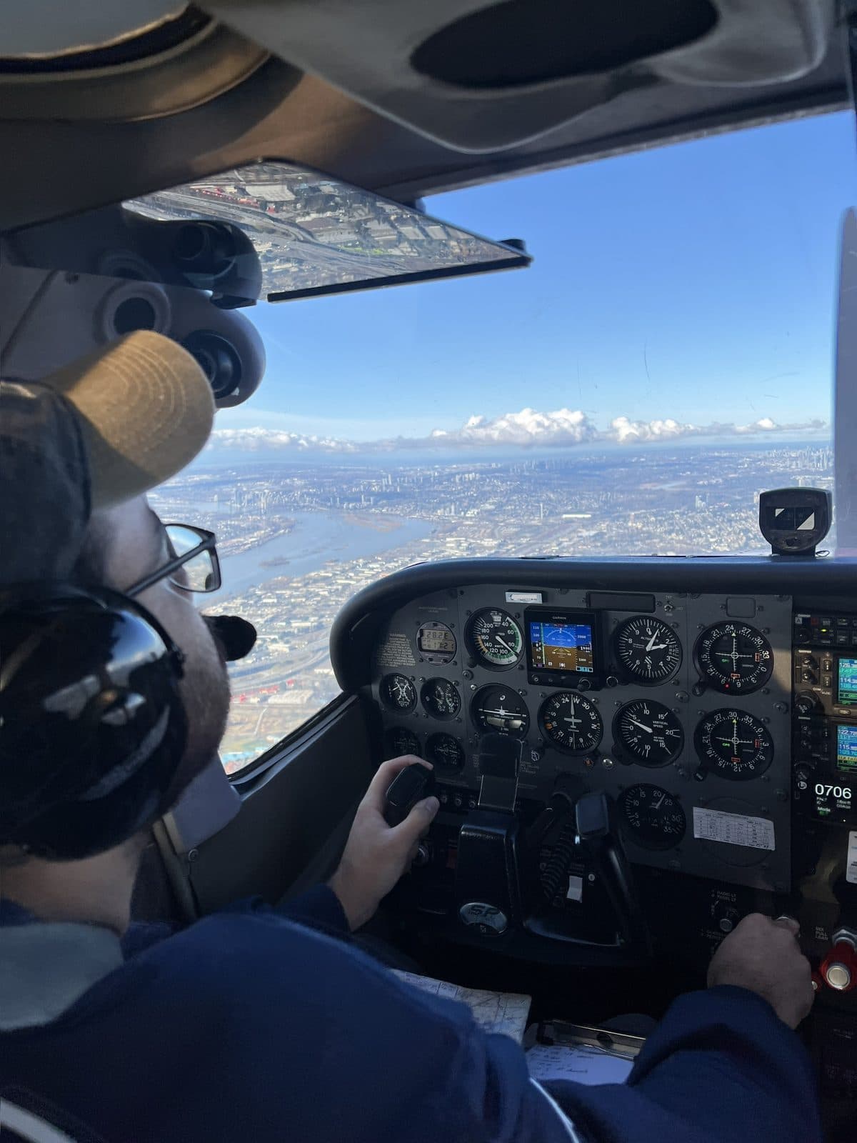 From behind the left seat of a light aircraft: a student flying with the Fraser River, Vancouver and the North Shore mountains spread out ahead through the windscreen.